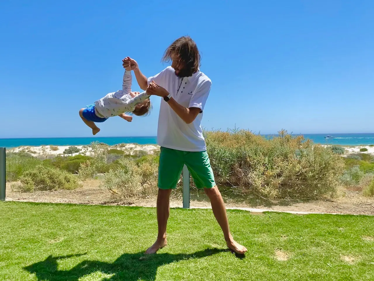 Папа и сын играют у океана, папа крутит ребенка